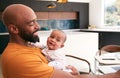 Smiling Stay At Home African American Father Cuddling Baby Daughter Whilst Working On Laptop At Home Royalty Free Stock Photo