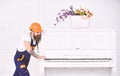 Smiling strong man with stylish beard and mustache trying to move old wooden piano with flower vase. Handsome worker in