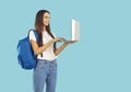 Smiling student girl with backpack in casual clothes working on laptop on light blue background. Royalty Free Stock Photo