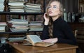 Smiling student girl in glasses in the library studying and day dreaming, she is thinking with hand on chin and looking Royalty Free Stock Photo