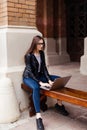 Smiling student girl sitting on bench in park, working with laptop and taking notes, preparing for exams outdoors, having rest in Royalty Free Stock Photo