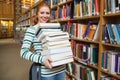 Smiling student holding heavy pile of books standing in library Royalty Free Stock Photo