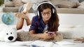 Smiling student teenage young girl uses mobile phone to listening the music, she wear headphones, schoolgirl studying lying on the Royalty Free Stock Photo