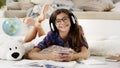 Smiling student teenage young girl uses mobile phone to listening the music, she wear headphones, schoolgirl studying lying on the Royalty Free Stock Photo