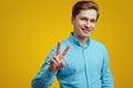 Smiling student wearing blue shirt and is gesturing vsign over yellow wall Royalty Free Stock Photo