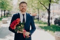 Smiling stylish stubbly gentleman in dark blue tuxedo with big bouquet