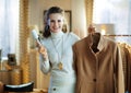 Smiling stylish woman cleaning coat on hanger with lint roller