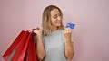 Smiling, stylish young blonde woman flaunts her shopping bags and credit card over vibrant isolated pink background, portrait of a