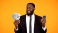 Smiling Successful black male in suit holding phone and dollar bills, cashback