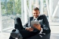 Smiling successful businessman in elegant suite using tablet sitting on bean bag chair in creative office Royalty Free Stock Photo