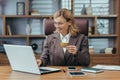 A smiling and successful businesswoman in a business suit works in the office at a laptop and makes financial Royalty Free Stock Photo