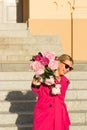 Smiling successful businesswoman in crimson dress and glasses holding bouquet of pink peonies. Small business concept.
