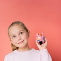 Smiling successful girl 5th in sweater holding piggy bank on palm isolated over pink background and looking up Royalty Free Stock Photo