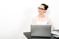 Smiling and successful woman wearing blouse and eyeglasses in sits at her desk with a laptop and looks away at the empty space.