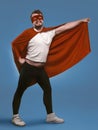 Smiling super hero man ready to fly save world. Funny man in red superhero costume and mask holding his cloak with hand Royalty Free Stock Photo