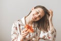 Smiling sweet girl in pajamas, holding a piece of pizza in her hands and looking into the camera on a light background. Close up Royalty Free Stock Photo