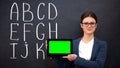 Smiling teacher holding prekeyed tablet, alphabet on blackboard, innovations