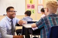 Smiling teacher kneeling beside elementary school pupilÃ¯Â¿Â½s desk