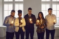 Smiling team looking at glowing lightbulbs in hands stand over office background
