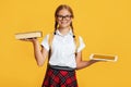 Smiling teen european blonde female in glasses weighs book and tablet in hands