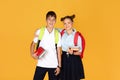 Smiling teen european girl with backpack hugs boy with notebooks, isolated on yellow studio background Royalty Free Stock Photo