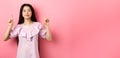 Smiling teen girl asian pointing fingers up at empty space, advertising on pink background