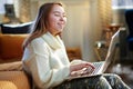 Smiling teen girl typing message while sitting near couch Royalty Free Stock Photo