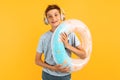 Smiling teen guy, with an inflatable swimming circle, listening to music on headphones, standing on an yellow background Royalty Free Stock Photo