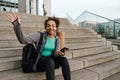 Smiling african girl using mobile phone and waving hand while sitting with yoga mat outdoors Royalty Free Stock Photo