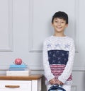 Smiling teenage Asian boy holding book bag standing beside desk Royalty Free Stock Photo