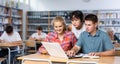 Smiling teenage boy and girls using laptop at library, watching videos Royalty Free Stock Photo