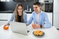 Smiling teenage boy holding glass with juice and using laptop accompanied with his girl friend at home. Royalty Free Stock Photo