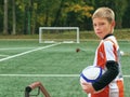 Smiling teenage boy with a soccer ball in his hand and soccer boots on the shoulder against the background of the Royalty Free Stock Photo