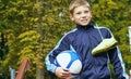 Smiling teenage boy with a soccer ball in his hand and soccer boots on the shoulder against the background of the Royalty Free Stock Photo