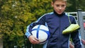 Smiling teenage boy with a soccer ball in his hand and soccer boots on the shoulder against the background of the Royalty Free Stock Photo