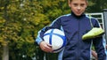 Smiling teenage boy with a soccer ball in his hand and soccer boots on the shoulder against the background of the Royalty Free Stock Photo