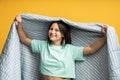 Smiling teenage girl in blanket isolated on yellow. Happy girl enjoys comfort coziness in soft duvet