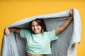 Smiling teenage girl in blanket on yellow. Happy girl enjoys comfort coziness in soft duvet