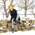 Smiling teenage girl cleaning boot from snow on stone wall