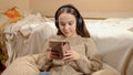 Smiling teenage girl listening music in headphones using tablet computer in her bedroom Royalty Free Stock Photo