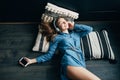 Smiling teenage girl with long hair lying at floor with pillow. Relaxing with cool music in headphone. Attractive student listenin