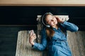 Smiling teenage girl with long hair lying at home interior and relaxing with cool music in headphone. Attractive student listening Royalty Free Stock Photo