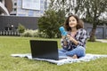 A smiling teenage girl sitting on the grass and using a laptop. A schoolgirl watches an Internet class and studies remotely. The