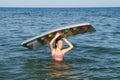 Smiling teenage girl standing in the sea and holding an inflatable mattress in her hands above her head Royalty Free Stock Photo