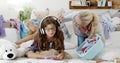 Smiling teenager girl with headphones listens to music and surfs the internet using a smartphone while her mother is scolding her Royalty Free Stock Photo