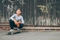 Smiling teenager skateboarder boy sitting beside a wooden grunge graffiti wall with skateboard and Water bottle flask. Youth