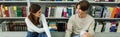 smiling teenagers talking near bookshelves in