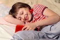 Smiling ten-year-old girl in a striped T-shirt with a phone in her hands lies on the bed, close-up Royalty Free Stock Photo