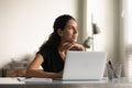 Smiling thoughtful female employee working at laptop from home