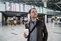 Smiling thoughtful man in front of arrivals and departures board at the airport with a coffee Royalty Free Stock Photo